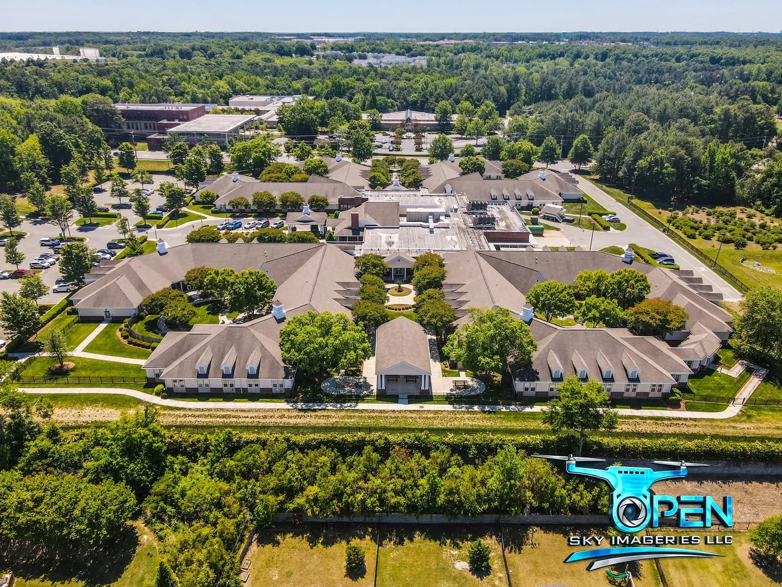 Aerial view of a campus with multiple buildings, parking areas, and surrounding trees.