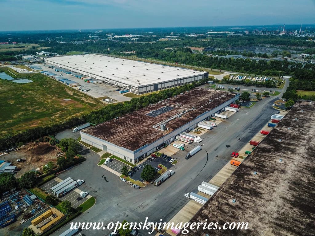 Aerial view of a large industrial building, parking, and surrounding land.