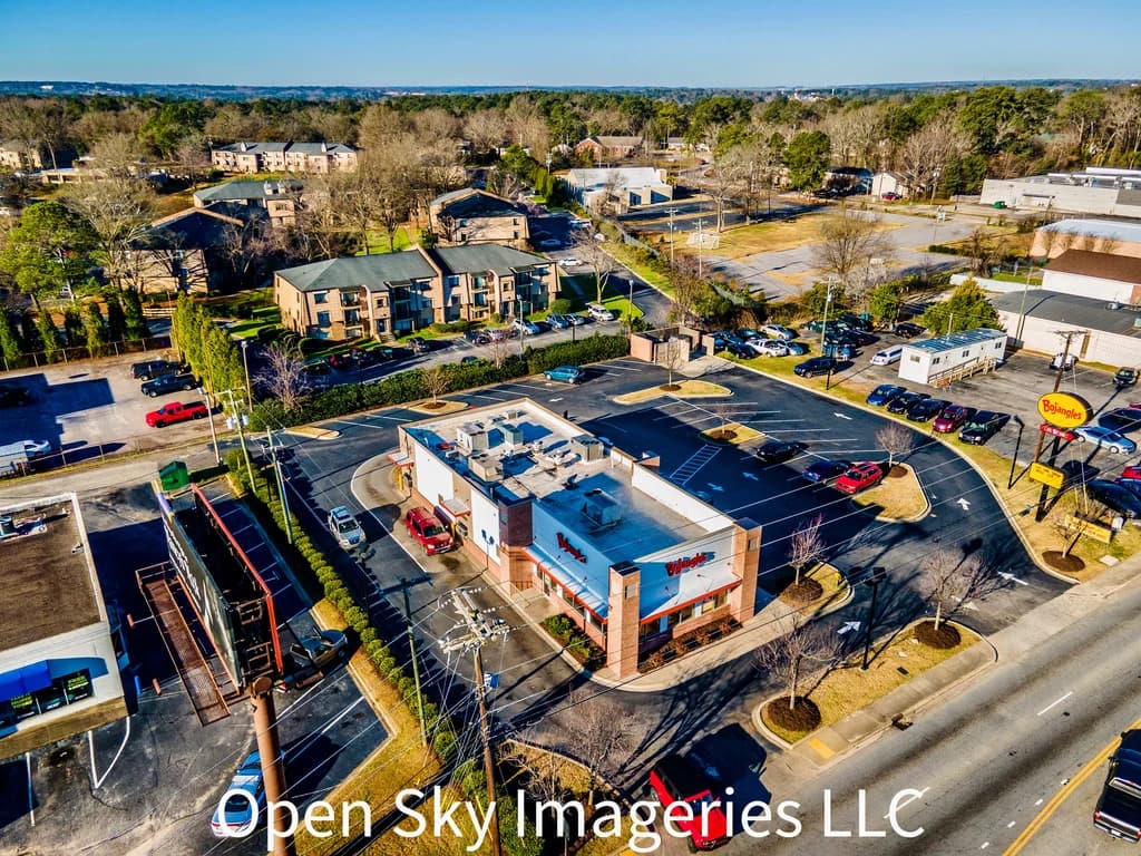 Aerial view of homes among tree-lined roads and open land.